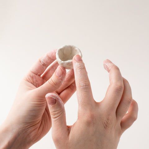 hands smoothing out the rim of a clay bell